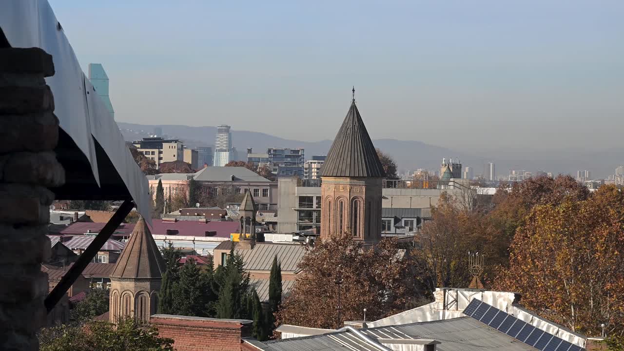 Wide cityscape view over Tbilisi in Georgia showing layered rooftops hills and riverside districts from an elevated viewpoint with soft evening light across the capital
