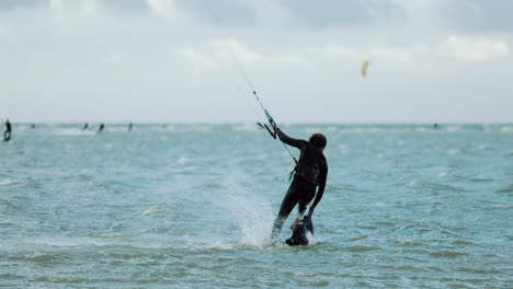 Kitesurfer-starting-his-session,-jumping-onto-kiteboard-on-blue-flat-water