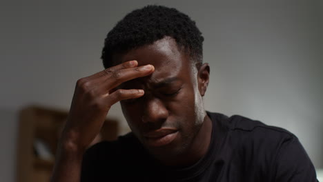 close up of unhappy and depressed young man sitting on sofa at home looking anxious and worried rubbing forehead 2