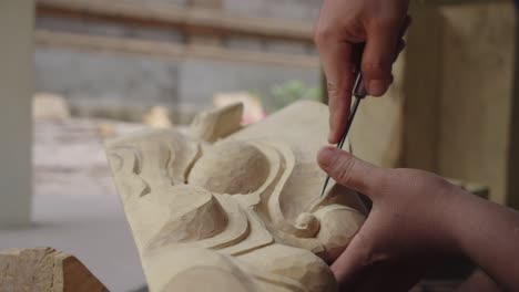 person shaping with a knife a wooden indonesian barong mask