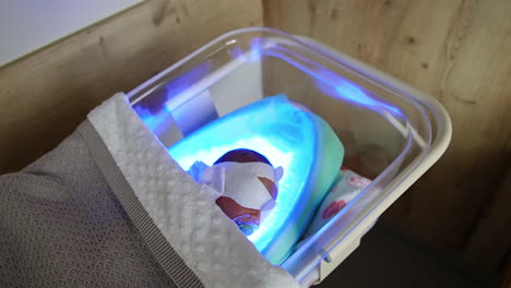 little baby with mask on eyes and with pacifier in mouth lies in the crib. newborn child undergoes the phototherapy against jaundice.