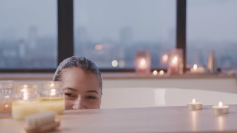 woman hiding behind a wooden table smiling at camera while taking a bath