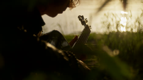 young musician playing guitar by the river at sunset