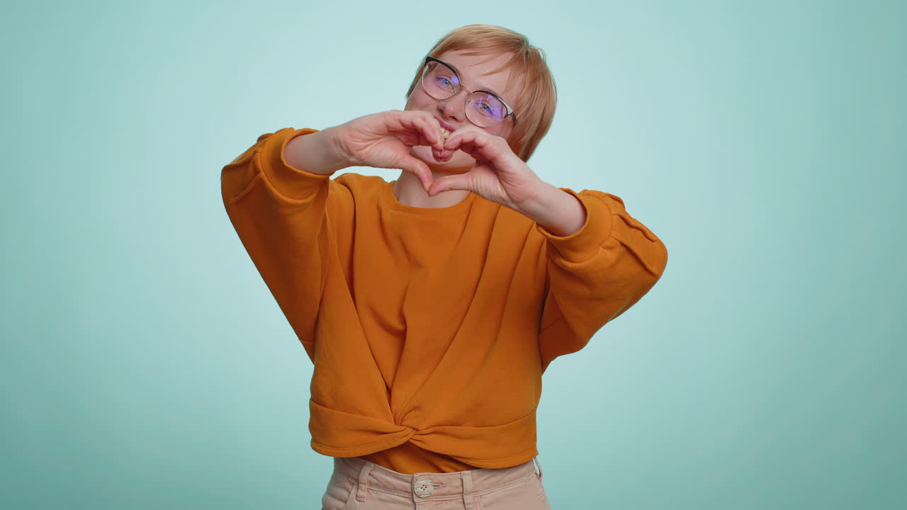 Smiling blonde woman makes heart gesture demonstrates love sign expresses good feelings and sympathy
