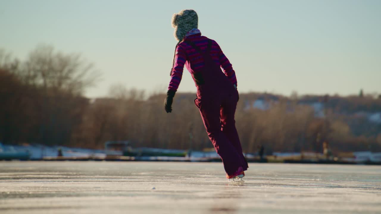 Una giovane skater scivola con grazia su un lago ghiacciato illuminato dal sole, mostrando le sue abilità e il suo entusiasmo per il pattinaggio sul ghiaccio, circondata da un pittoresco paesaggio invernale e da incantevoli case sullo sfondo.