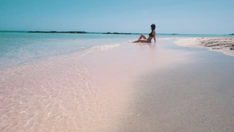 Eine-Frau,-Die-An-Einem-Rosafarbenen-Strand-Vor-Der-Türkisfarbenen-Lagune-Sitzt