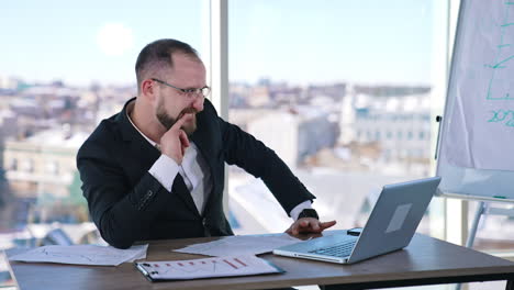businessman is out of mind in office. crazy male entrepreneur sitting at the table and gesticulating and typing on a laptop madly.