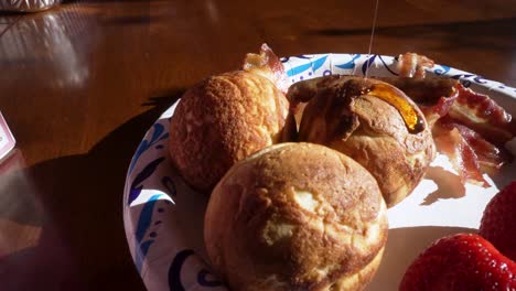 Drizzling-syrup-over-aebleskivers-on-a-plate-with-strawberries-and-beacon-in-slow-motion