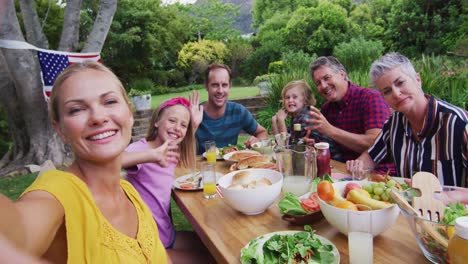 Smiling-caucasian-woman-taking-selfie-with-three-generation-family-having-celebration-meal-in-garden