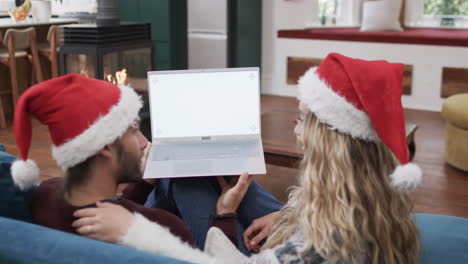 diverse couple wearing santa hats using laptop with copy space on screen, in slow motion