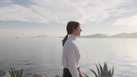 medium truck shot of a woman walking on a pier during golden hour and gazing upon the sea