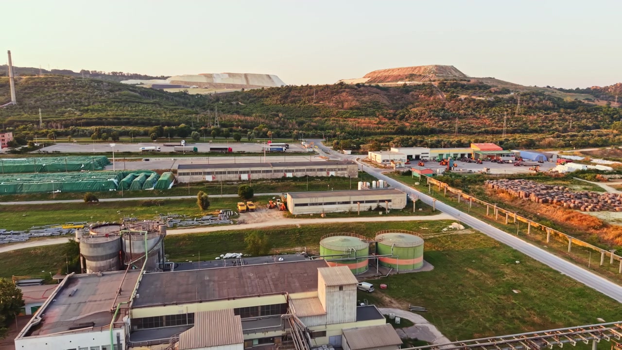 Large industrial site with storage tanks and green hills during sunset in a rural area