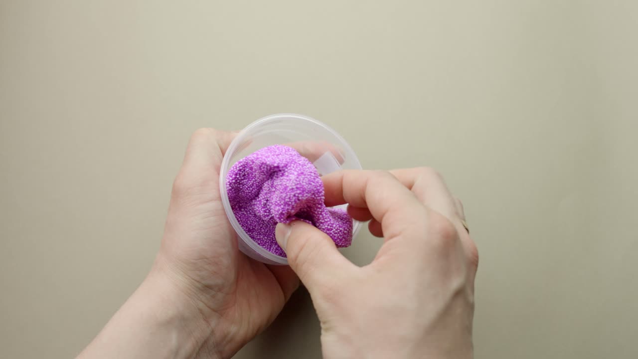 Floam slime is removed from a plastic cup and pushed and pulled by hand for ASMR effect.