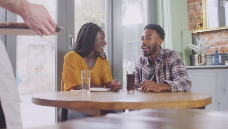 Waiter-In-Restaurant-Serving-Pizza-To-Couple-At-Table