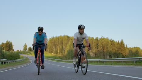 Two-professional-road-cyclists-ride-their-bikes-on-a-hill.-Hand-held-shot-of-two-strong-cyclists-female-and-male-on-their-training-on-a-warm-but-windy-summer-day