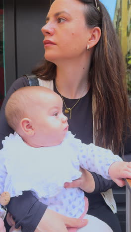 vertical video of a smiling young mother holding her baby girl on her lap in a candid outdoor moment. emotional family bonding scene with natural light and soft expressions