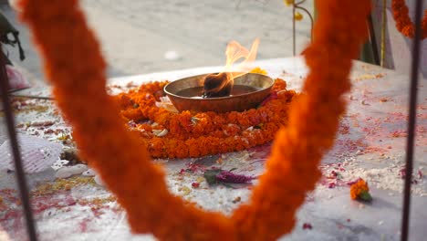 kathmandu, nepal - a fire is burning on the plate with oil decorated with flower garland as part of worship in front of a temple - close up