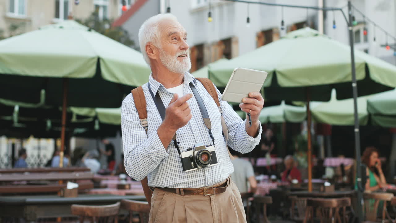 turista senior con cámara fotográfica de pie entre mesas con sombrillas