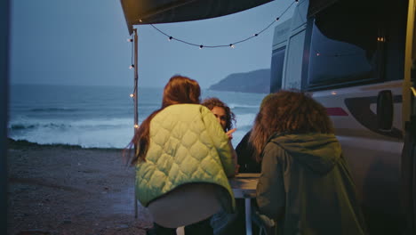 happy friends gathering camper van on gloomy evening ocean coast. women talking