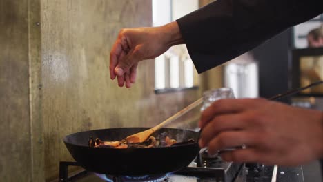 Mixed-race-male-chef-preparing-a-dish-and-smiling-in-a-kitchen-