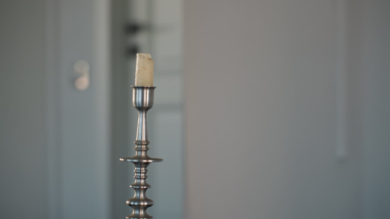 silver candle stand in front of large wall mirror reflecting closed door against neutral gray backdrop creating minimalist interior decor scene with soft natural ambient lighting and subtle shadow