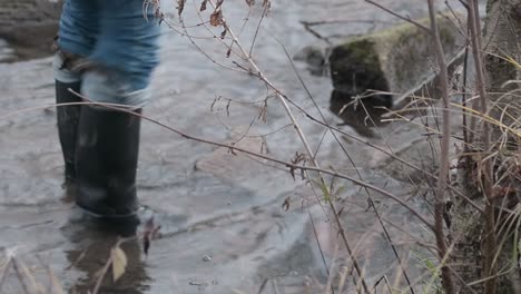 woman in wellington boots splashing in stream of water