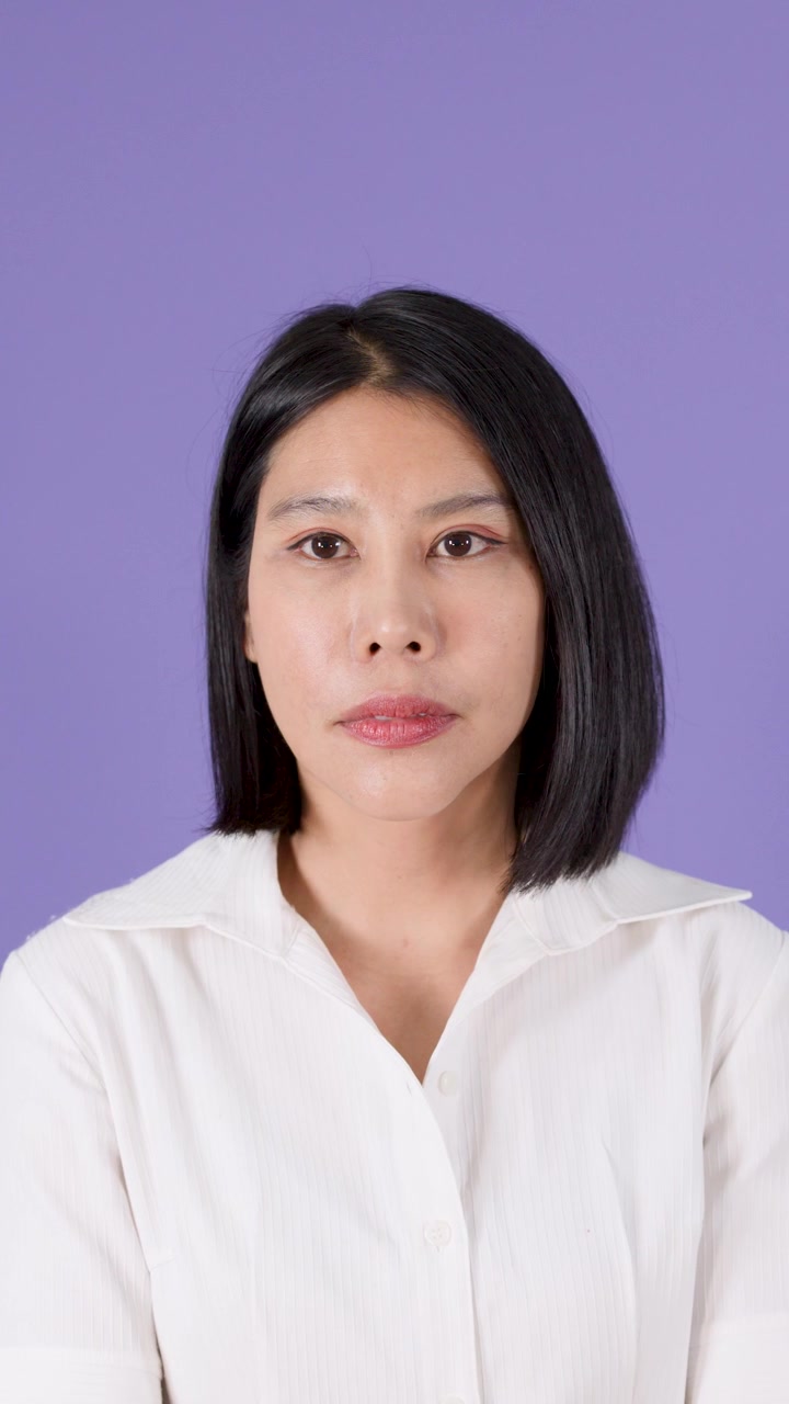 Seorang wanita Asia yang serius memeriksa jam tangannya dan terlihat khawatir dengan latar belakang ungu.