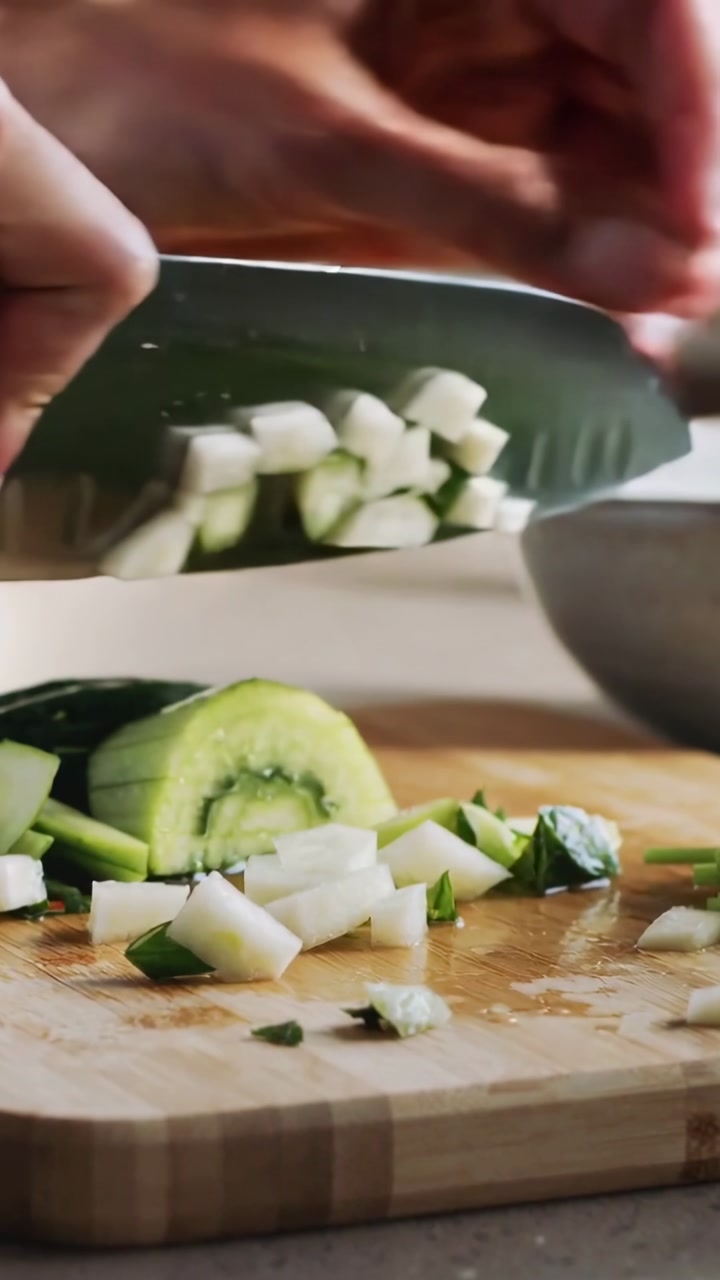 Vertical video: Knife slicing cucumber, hands dicing on board, sprinkling herbs for salad