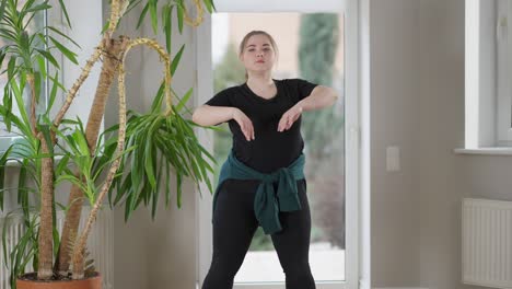 portrait of plump young woman doing chest circles warming up exercise indoors. confident positive plus-size lady training at home in the morning. fitness and healthy lifestyle concept