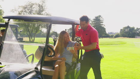 couple playing round on golf together sitting in buggy with score card