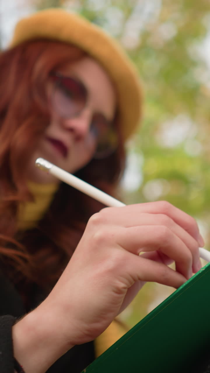 Primo piano di una mente talentuosa che schizza pensierosamente su tela con foglie autunnali sfocate sullo sfondo, con focus sull'espressione artistica, i tratti a matita e la profonda concentrazione.