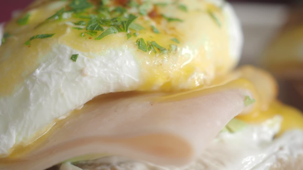 Close-up of a poached egg with hollandaise sauce and meat, possibly a variation of Eggs Benedict