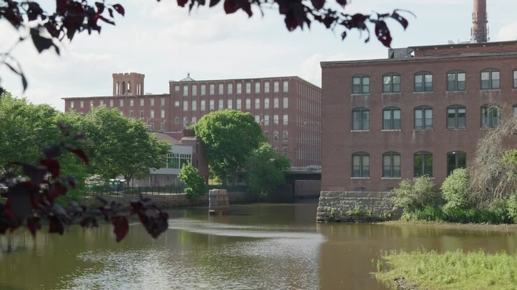 Una vista incorniciata da rami di acero rosso che mostra un edificio storico in mattoni rossi a Dover, NH, USA. Si trova su un fiume in una soleggiata giornata estiva
