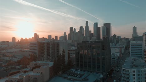 Vista-Cinematográfica-Del-Centro-De-Los-ángeles-Con-Un-Increíble-Resplandor-De-Puesta-De-Sol,-Drones-Elevándose-Sobre-Edificios