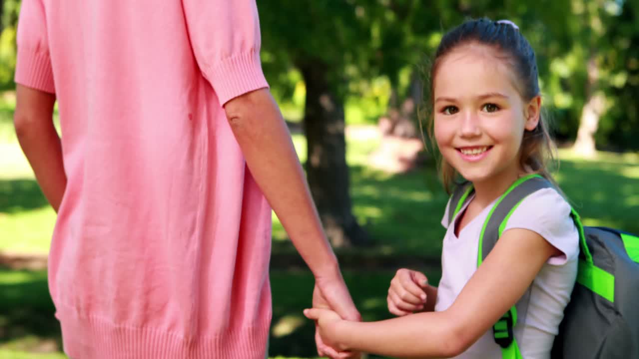 Madre che aspetta con la sua figlia sorridente il primo giorno di scuola.