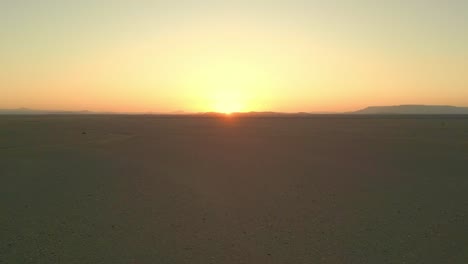 Aerial-drone-view-of-serene-desert-sunset-over-a-vast-horizon,-capturing-the-tranquil-beauty-of-the-desert-landscape-at-dusk-in-Saudi-Arabia