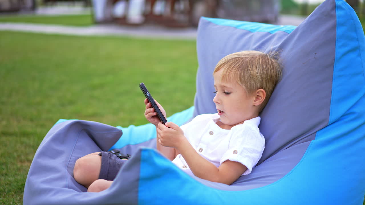 Child using a smartphone in a bean bag chair outdoors