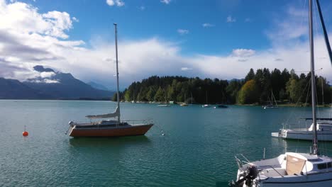 aerial view flying at low altitude sideways above huge lake passing by small sailing boats at forggensee in bavaria, germany in 4k