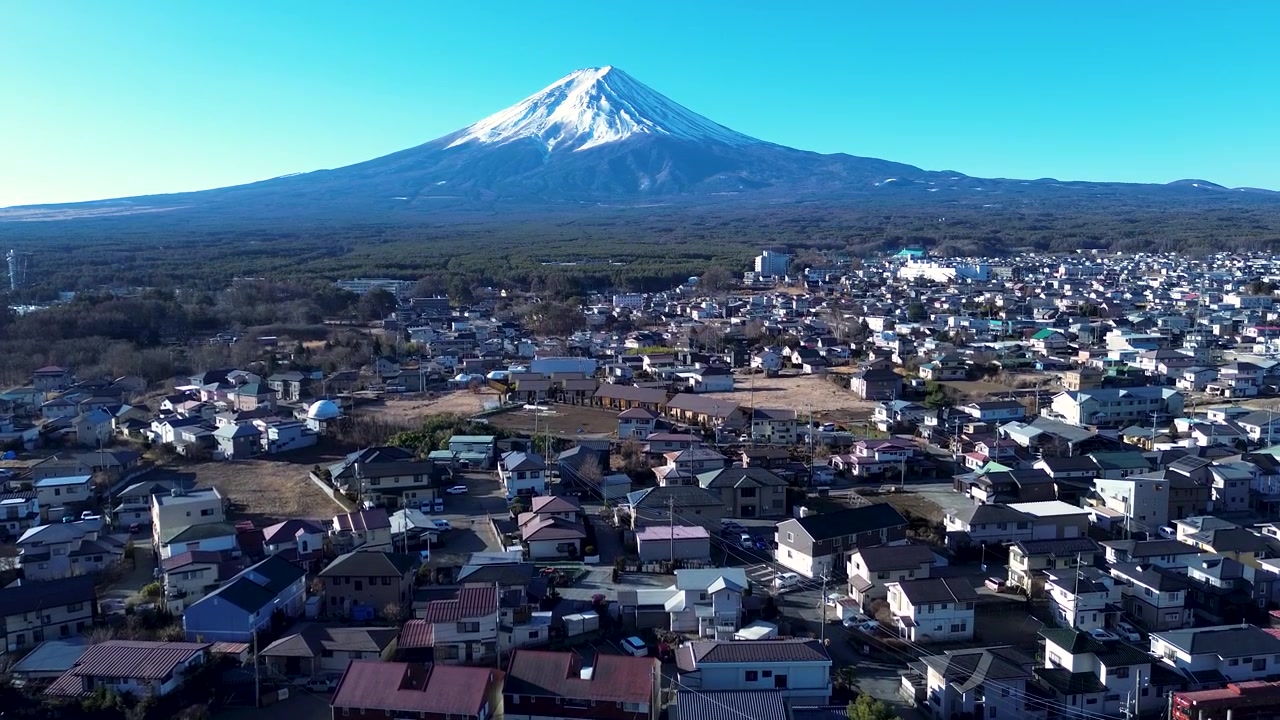 Drone-ilmakuva upeasta Fujivuoren maamerkkihuipusta, josta avautuu näkymä Kawaguchikon kaupunkiin ja kylään asuinrakennuksineen ja kaupunkikatuineen Minamitsurun alueella Japanissa. Aasian matkailu ja turismi.