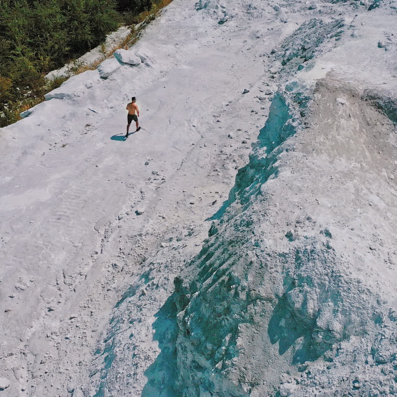 Sportsman in a white canyon exercising. Healthy athlete is running on the rocky hill in a sunny summer day. Aerial view.