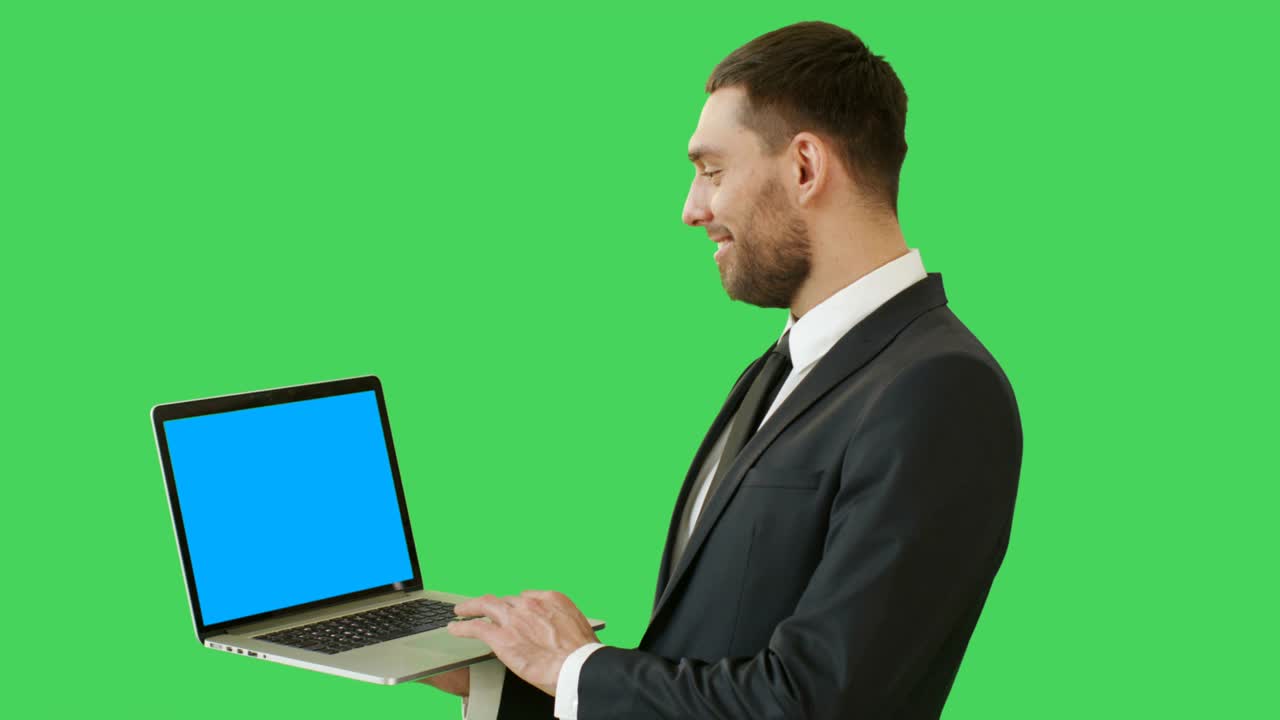 una toma media de un hombre de negocios guapo sosteniendo una computadora portátil trabajando con un touchpad. vemos la pantalla azul de la computadora portatil, todo filmado en un fondo de pantalla verde.