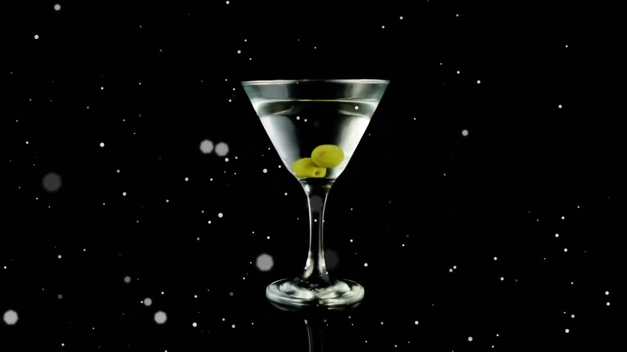 Punti bianchi che fluttuano su olive in un bicchiere da cocktail su sfondo nero.