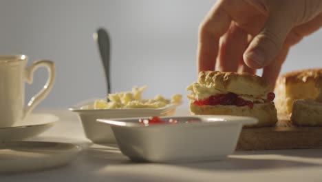 close up shot of person with traditional british afternoon tea with scones cream and jam