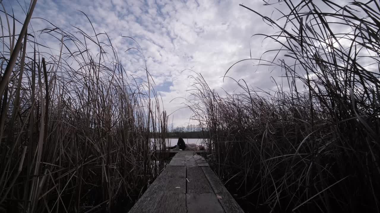 젊은이가 나무로 된 보행자 다리 위에 혼자 누워서 호수를 쳐다보고, 삶에 대해 생각하고, 자연에서 평화로운 분위기를 누리고, 신선한 공기를 즐기고, 뒤를 바라보고 있습니다.