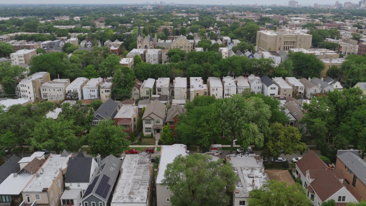 Riprese drone sui tetti densi di Chicago e strade alberate, con un parcheggio e un campanile di chiesa visibile in lontananza sullo sfondo