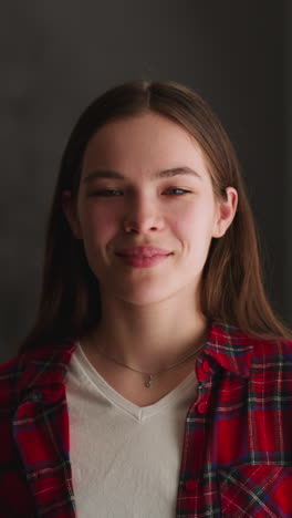 positive young woman in red casual flannel shirt smiles looking into camera in living room at home closeup slow motion. female model portrait indoors