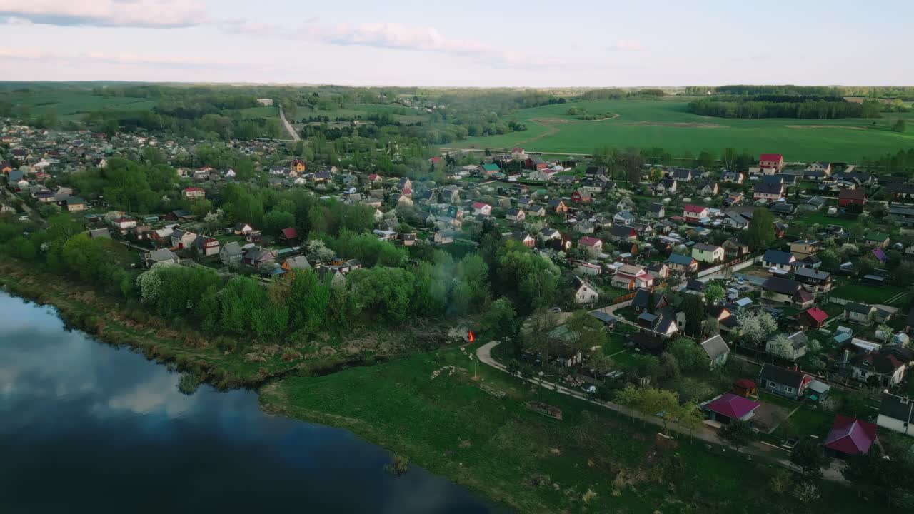 High-angle view of Malutki’s houses and orchards lining the Daugava River, merging into expansive farmland and forest. Malutki, Latvia (Malutki, Latvija)