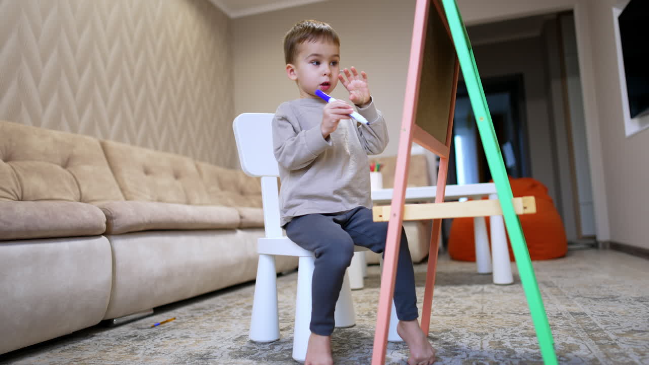 Young child drawing on art easel at home. A child focuses on drawing with markers on an easel in a cozy living room filled with natural light