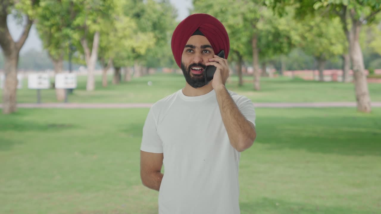 Uomo indiano Sikh felice che parla al telefono e sorride al parco