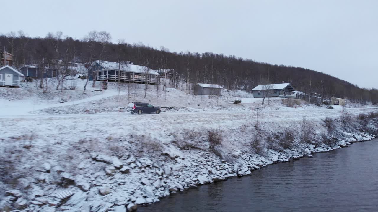 스웨덴 라플란드의 가혹한 북유럽 풍경 속에서 호숫가 도로를 여행하는 자동차 - 공중 추적 낮은 각도 샷